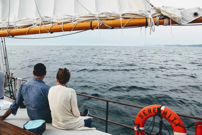 Two people sitting at the rail of the schooner Serenity looking out over open water, a life ring marked SERENITY beside them